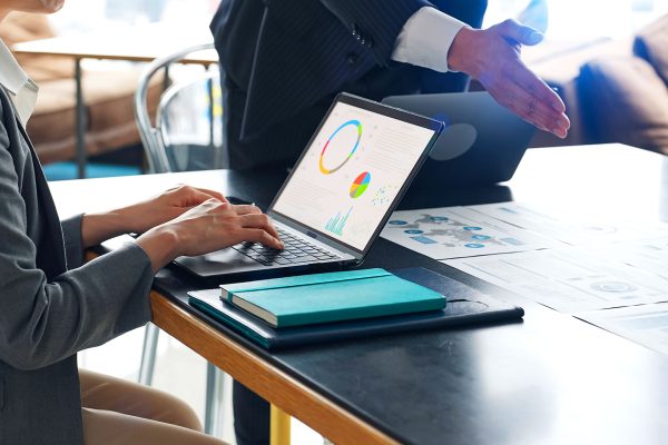 Business professional reviewing data charts on laptop with printed reports on desk