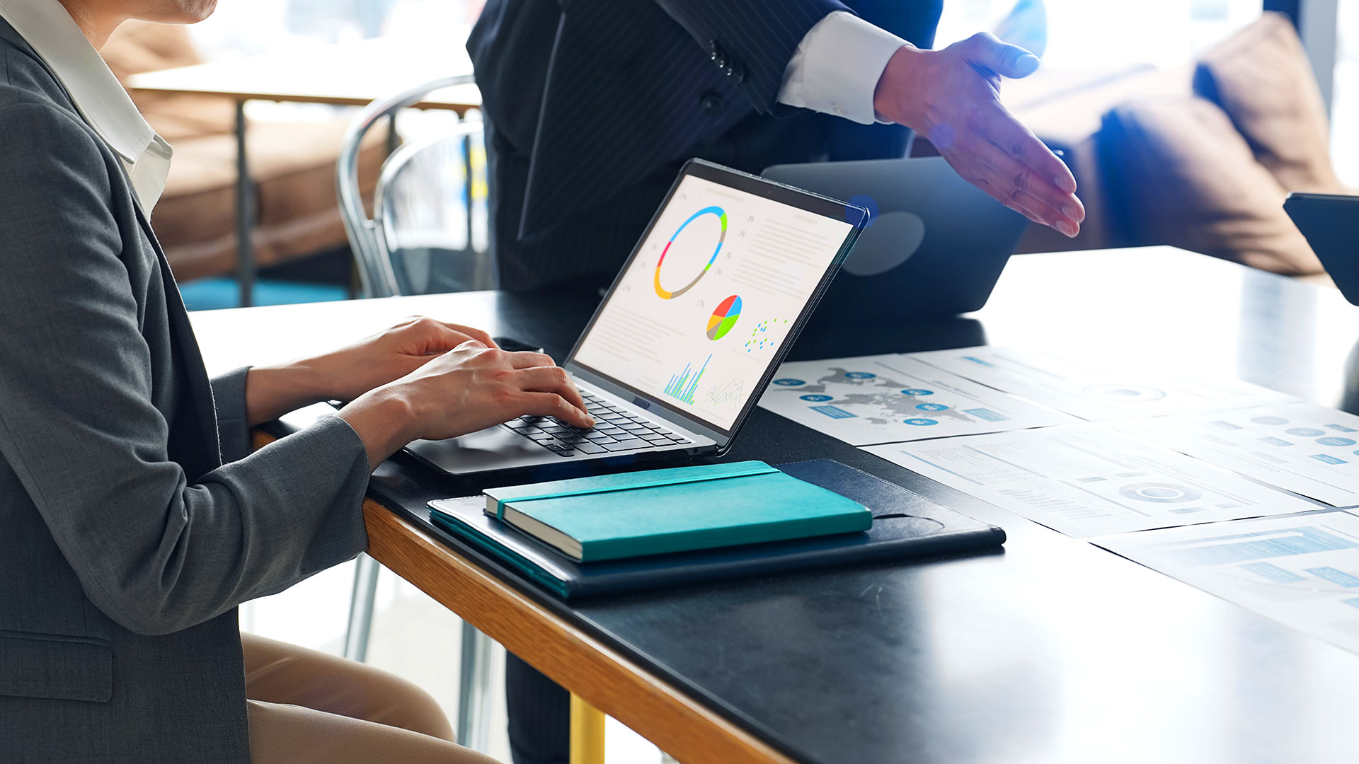 Business professional reviewing data charts on laptop with printed reports on desk