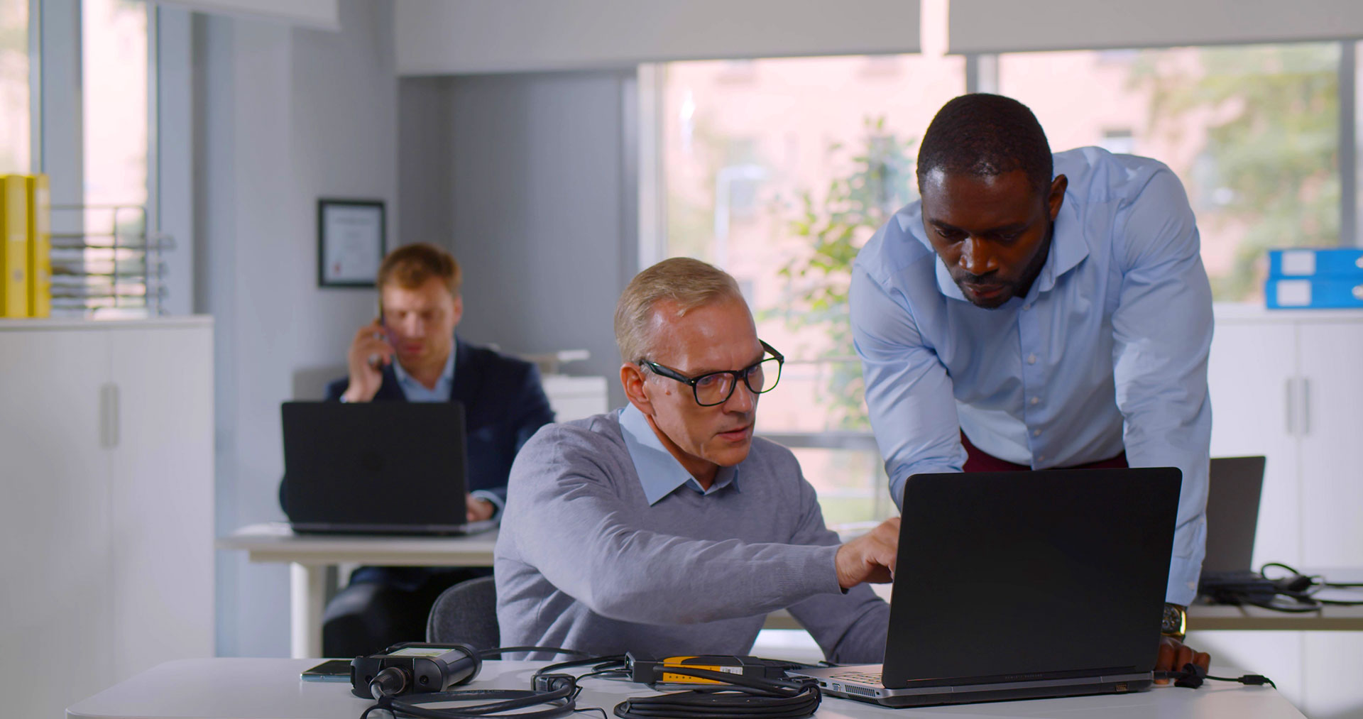 Two IT technicians troubleshooting a laptop with network cables in office environment